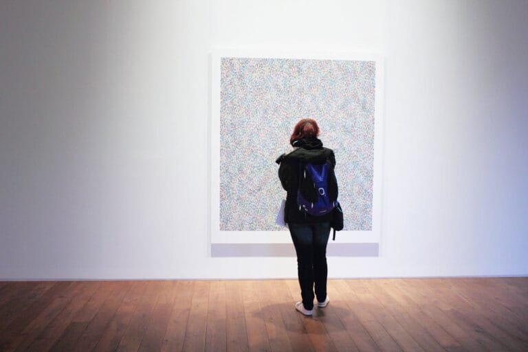 A woman with a backpack observes a colorful painting in an art gallery.